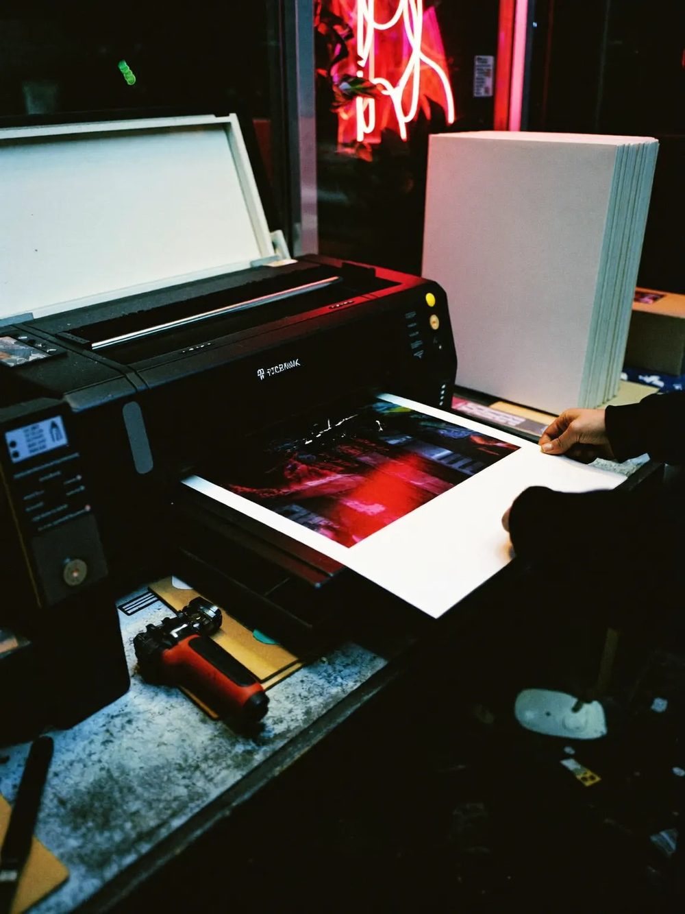 A print being trimmed and checked on the bench under neon light